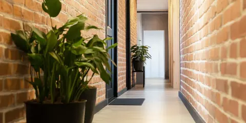 Przedpokój loft inspiracje: ceglane ściany, jasna podłoga i zielone rośliny tworzą przytulną atmosferę.