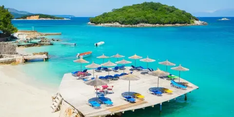Idealne miejsce, gdzie na wakacje nad morze: piaszczysta plaża, turkusowa woda, leżaki i parasole na drewnianym pomoście.