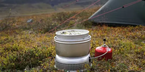 Matlagning på ett esbit kök i fjällen. En kastrull med mat värms upp bredvid ett tält.