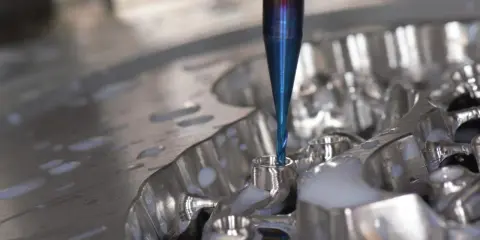 Fresa blu lavora un pezzo metallico, creando dettagli precisi. La cam meccanica è in azione, con liquido refrigerante che schizza.