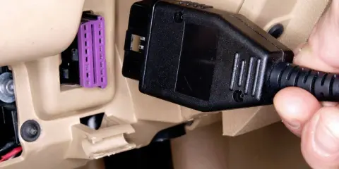 Ręka podłącza kabel do gniazda OBD w samochodzie, aby sprawdzić jego stan.