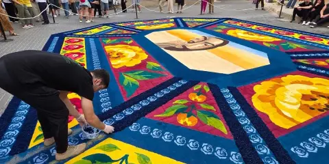 Un hombre finaliza una de las alfombras de serrín de Elche de la Sierra, con un retrato central y motivos florales y frutales.