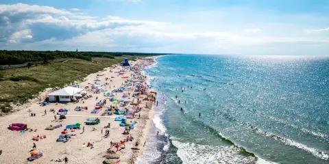 Tłum ludzi na plaży w Darłowie, korzystających z uroków lata. Wiele kolorowych parawanów i namiotów, a w wodzie kąpielowicze. To idealne darłowo atrakcje dla każdego.