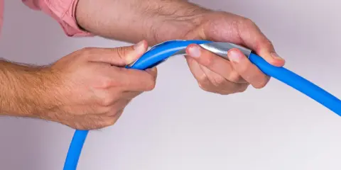 Mains bleues tenant un tuyau bleu avec un outil métallique pour former un coude boule.