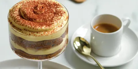 Delizioso tiramisù senza caffè, stratificato con crema e cacao, accanto a un espresso.