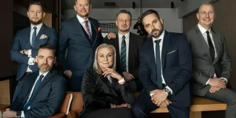 Grupa siedmiu profesjonalistów w garniturach, w tym jedna kobieta, pozuje do zdjęcia.