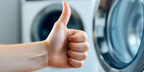 Pouce levé devant une machine à laver, signe d'un branchement machine à laver réussi.