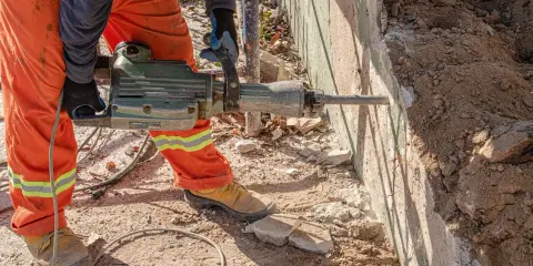 Trabajador con martillo neumático realiza demolición manual de muro de hormigón.