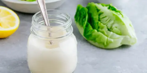 Un pot de vrai sauce césar crémeuse, avec une feuille de laitue romaine et un quartier de citron.