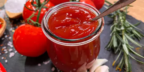 Ein Glas hausgemachtes Ketchup, das Zutaten für das beste Ketchup Rezept: Tomaten, Knoblauch, Rosmarin, Salz und Gewürze.