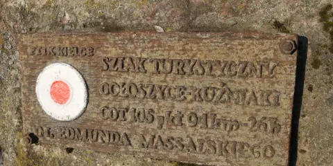 Tabliczka na skale z czerwono-białym kołem i napisem "Główny szlak świętokrzyski im. Edmunda Massalskiego".