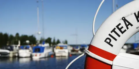 Livboj med texten PITEÅ K visar en hamn med båtar. Ett perfekt ställe att besöka Piteå på!