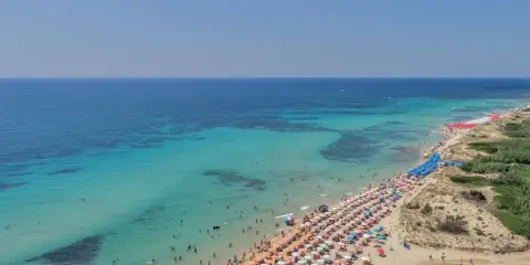 Spiaggia affollata con ombrelloni colorati e acque cristalline, le Maldive della Puglia dove si trovano per godersi il sole e il mare.