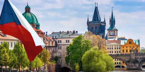 Flaga Czech powiewa nad Pragą, ukazując ciekawe fakty o Czechach. W tle widać Most Karola i wieże.
