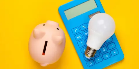 Hucha rosa, calculadora azul y bombilla LED. Ideas para como ahorrar en la factura del gas y la luz.