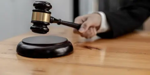 Mano che impugna un martelletto da giudice, pronto a battere sul ceppo. Il suo significato, il g.u.p., è un momento cruciale.