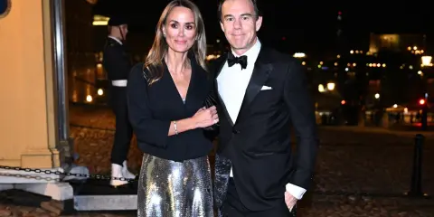 A couple in formal attire poses at night with a blurred city background.