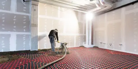 Un ouvrier installe un système de chauffage au sol hydraulique. Des tuyaux rouges serpentent sur une grille noire, prêts à diffuser une chaleur douce.