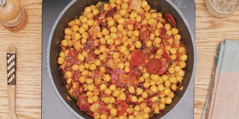 Garbanzos fritos con chorizo y bacon en sartén, listos para servir. Un plato sabroso y reconfortante.