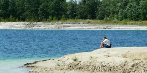 Samotny mężczyzna siedzi na brzegu, kontemplując turkusową wodę. To spokojne miejsce, jakby zapomniany osadnik gajówka.