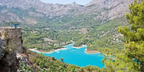 Espectacular vista de la ruta pueblos interior Alicante, con un embalse turquesa rodeado de montañas y vegetación.