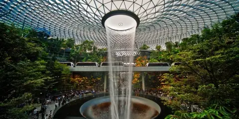 Wodospad HSBC Rain Vortex w porcie lotniczym Singapur-Changi, otoczony bujną zielenią i przejeżdżającymi pociągami.