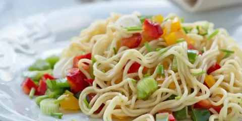 Ein bunter asia nudelsalat mit Paprika und Frühlingszwiebeln auf einem weißen Teller.