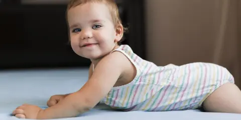 Un adorabile neonato di 8 mesi, con occhi azzurri e un sorriso contagioso, gioca sul letto.