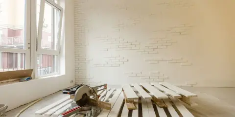 Herramientas listas para como pintar un palet. Madera blanca apilada, sierra ingletadora y pared con ladrillos blancos.