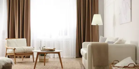 Salon cosy avec 1 ou 2 rideaux par fenêtre, fauteuil en bois, canapé blanc, table basse et tapis en jute.