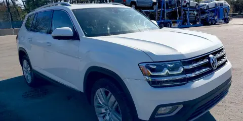 Biały VW Atlas stoi na parkingu, w tle widać lawetę z innymi samochodami.