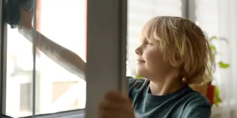 Chłopiec z uśmiechem na twarzy wykonuje jedno z domowych obowiązków – myje okno.