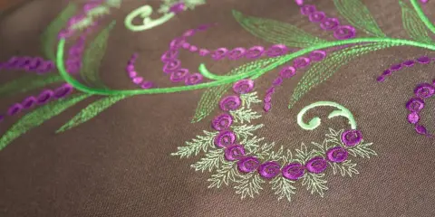 Haftowane wzory kwiatowe w kolorach zielonym i fioletowym na brązowym tle.