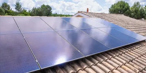 Panneaux solaires bleus brillants sur un toit de tuiles, sous un ciel bleu avec des nuages blancs. Une installation photovoltaïque autonome pour une énergie verte.