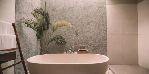 Relajante bañera exenta rodeada de piedras blancas, toallas dobladas en una escalera de madera y una planta tropical. Un ejemplo de cuartos de baño modernos y serenos.