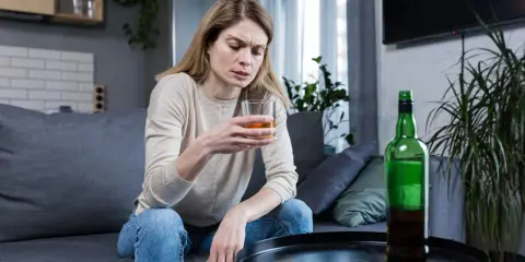 Kobieta z kieliszkiem alkoholu i butelką obok. Obraz symbolizuje 10 strat z picia alkoholu, pokazując jej smutek i zagubienie.