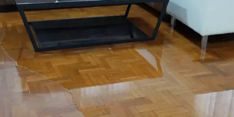 Un salon inondé, le parquet gondolé par l'eau. Une table basse et un pouf flottent dans le désastre.