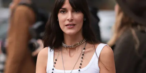 Frau mit langen Haaren und Curtain Bangs, trägt weiße Tanktop und Chanel-Schmuck.
