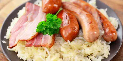 Assiette de choucroute allemande ou alsacienne garnie de saucisses et de lardons, décorée d'une touche de persil frais.