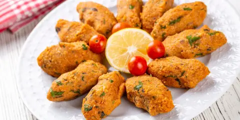 Deliziose polpette di lenticchie, disposte a cerchio su un piatto bianco, con spicchi di limone e pomodorini ciliegino.