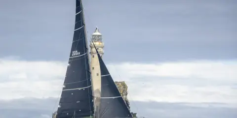 Segelboot mit schwarzen Segeln navigiert durch raue See am Fastnet Rock, ein dramatischer Moment im Fastnet Race.