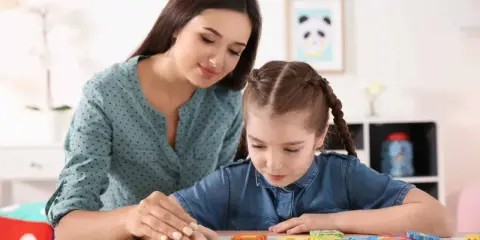 Terapeuta pomaga dziecku z niepełnosprawnością intelektualną układać kolorowe puzzle.