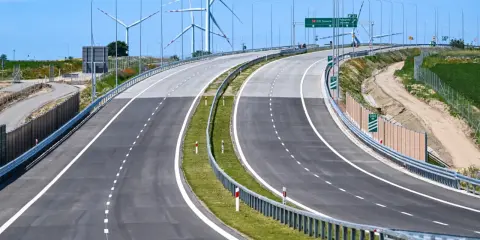 Nowa droga S6 z wiatrakami w tle. Pusta autostrada z zielonym pasem zieleni i barierami.