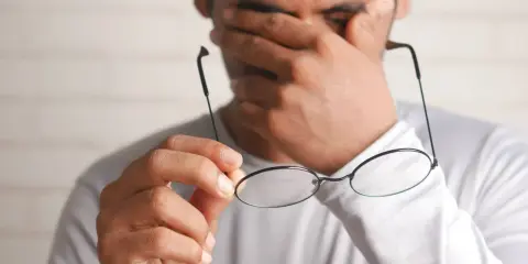 Mężczyzna pociera oczy, trzymając okulary.
