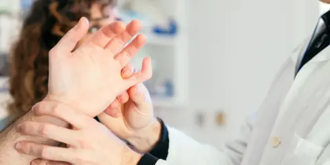 Lekarz bada dłoń pacjenta, który skarży się na bolące stawy.