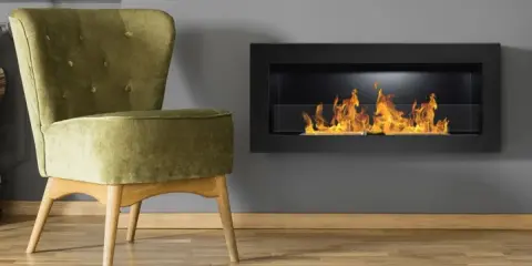 Sillón verde junto a chimenea moderna encendida. Un ejemplo de como encender la chimenea para crear un ambiente acogedor.