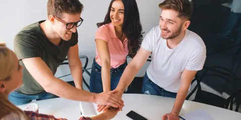 Equipo unido en formación de gestión de equipos. Jóvenes sonríen mientras juntan sus manos en señal de compromiso y colaboración.