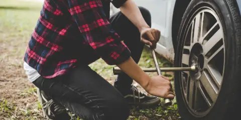 Osoba w kratę naprawia koło po otarciu felgi o krawężnik.