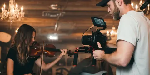Un caméraman s'apprête à créer un clip vidéo, filmant une violoniste et un guitariste dans un décor chaleureux avec des lustres.