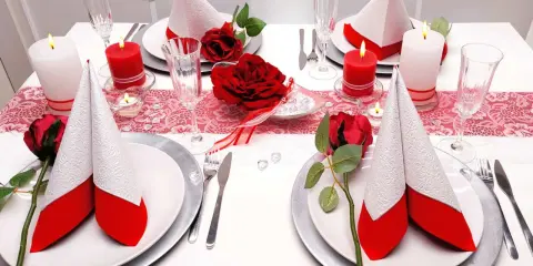 Festlich gedeckter Tisch für eine rot-weiße Hochzeit. Rote Rosen und Kerzen sorgen für romantische Stimmung.